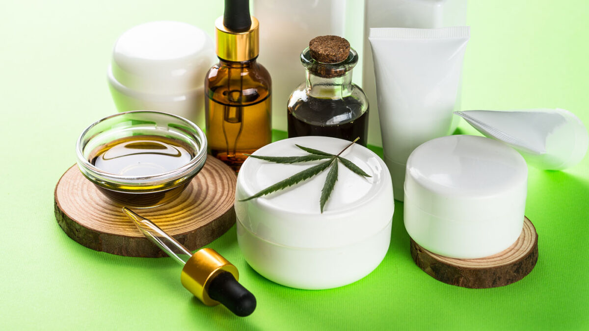 Cannabis cosmetic products at green background. Natural cosmetic concept. Cream, soap, serum, essential oil and others.